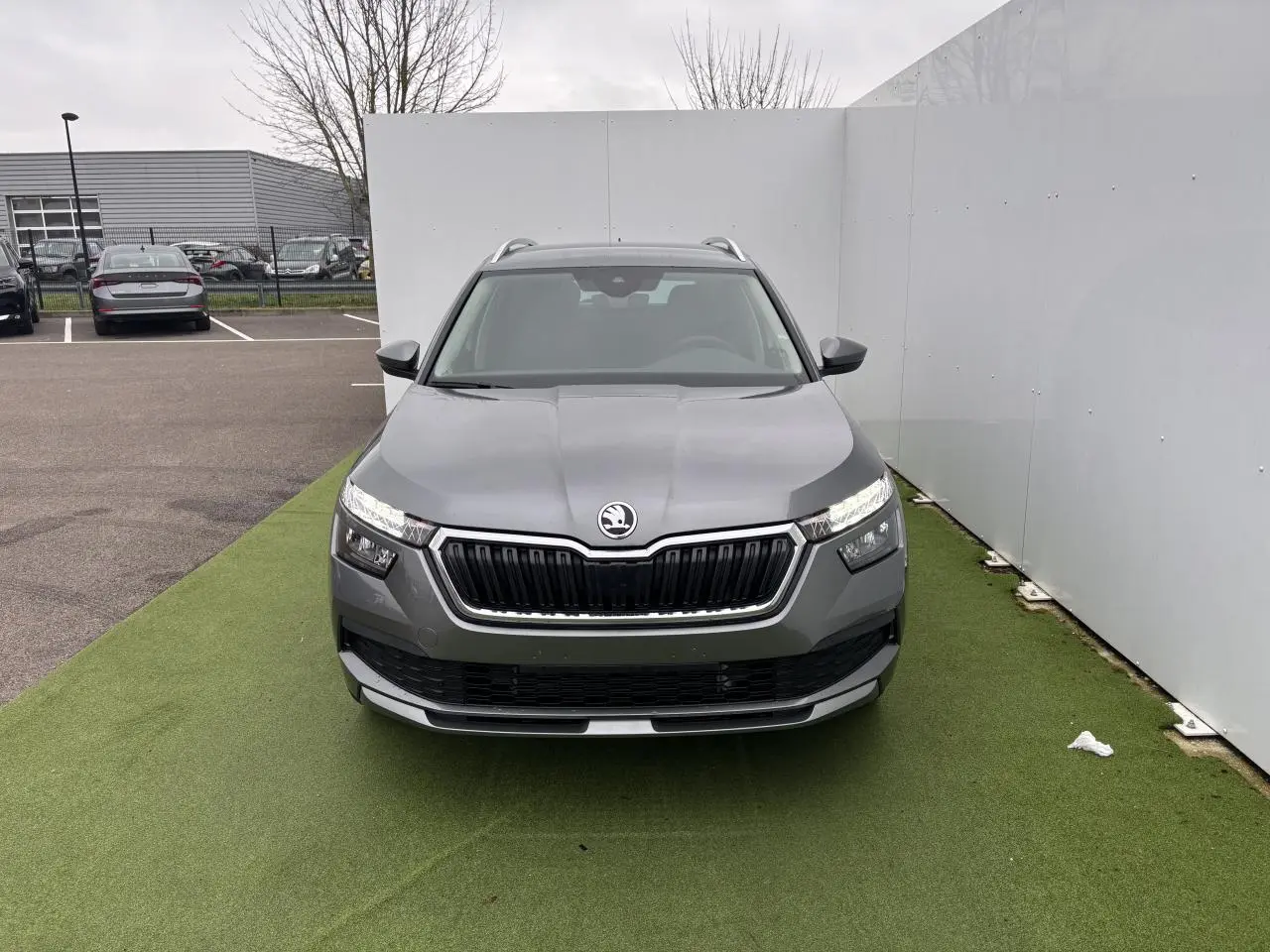 Vue avant d'un Skoda Kamiq gris graphite métal avec calandre noire et feux LED allumés sur fond urbain.