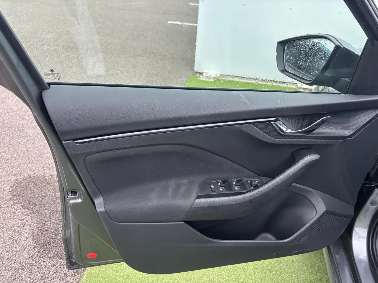 Porte avant gauche ouverte du Skoda Kamiq gris graphite, montrant les commandes des vitres et la poignée intérieure noire.