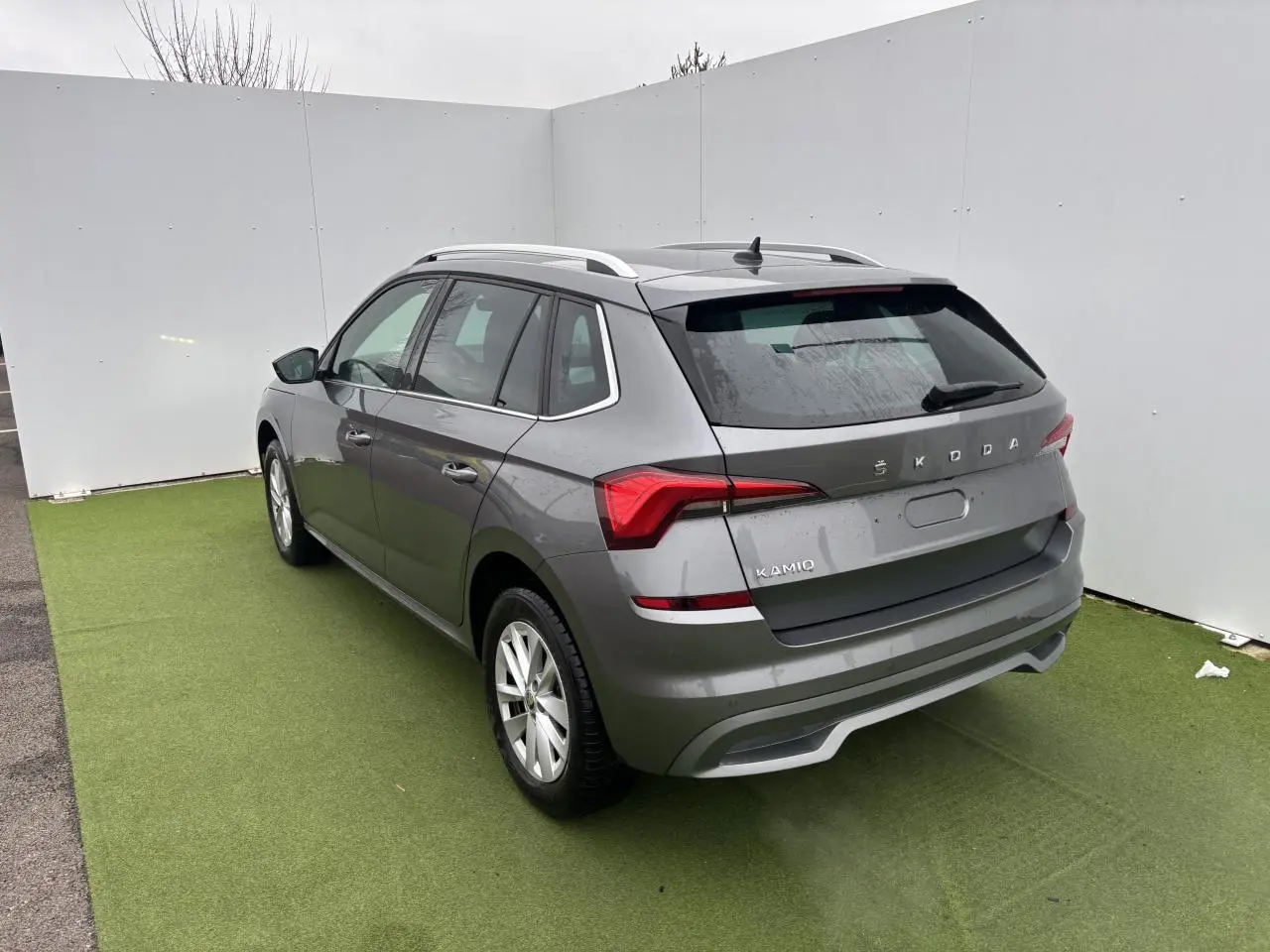 Vue 3/4 arrière droite d'un Skoda Kamiq gris graphite métallisé avec feux arrière LED et barres de toit argentées.