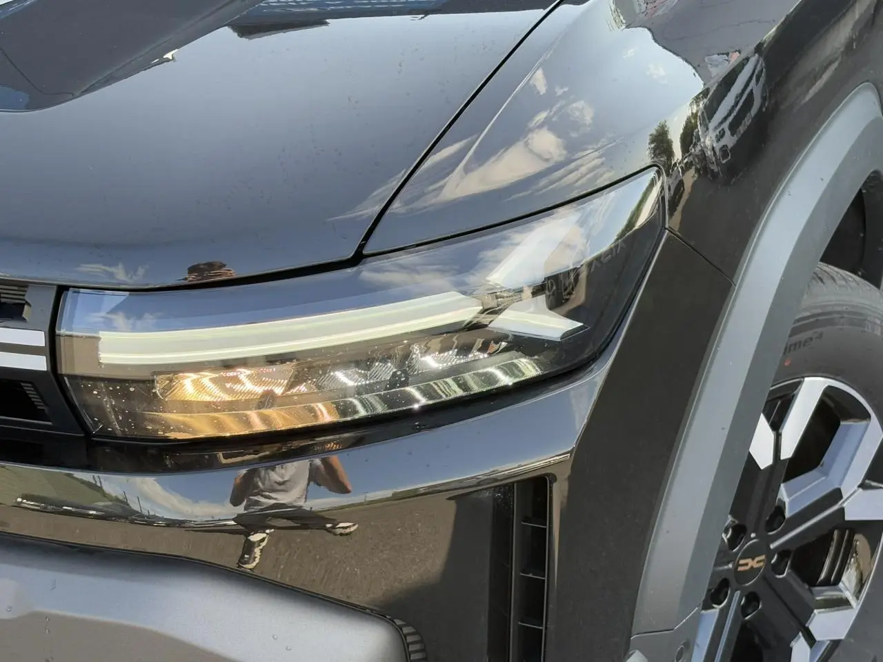 Gros plan sur le phare avant droit et la roue alliage 17" du Dacia Duster noir nacré 2025.