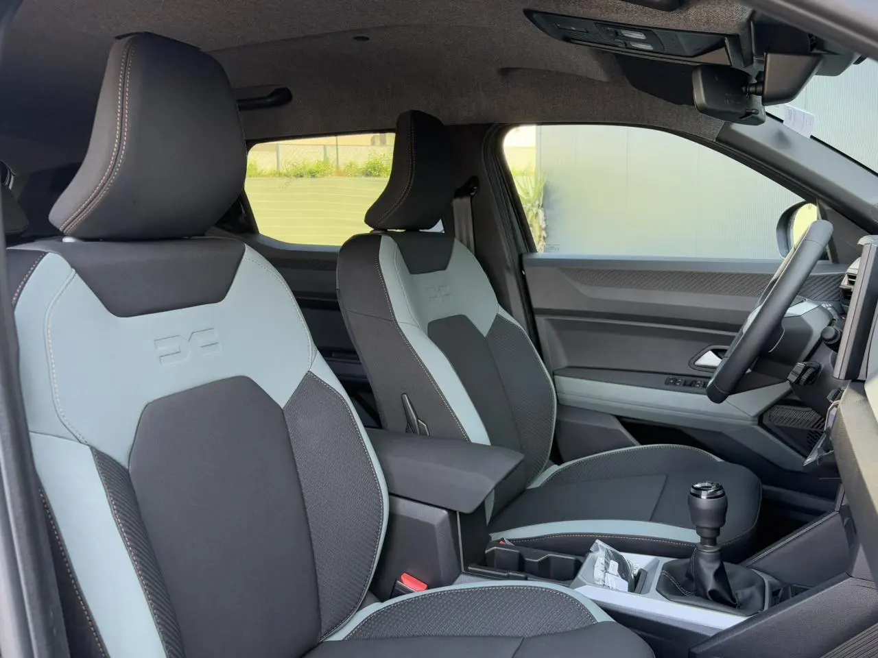 Vue intérieure côté conducteur du Dacia Duster 2025, sièges bicolores avec surpiqûres et levier de vitesses manuel.