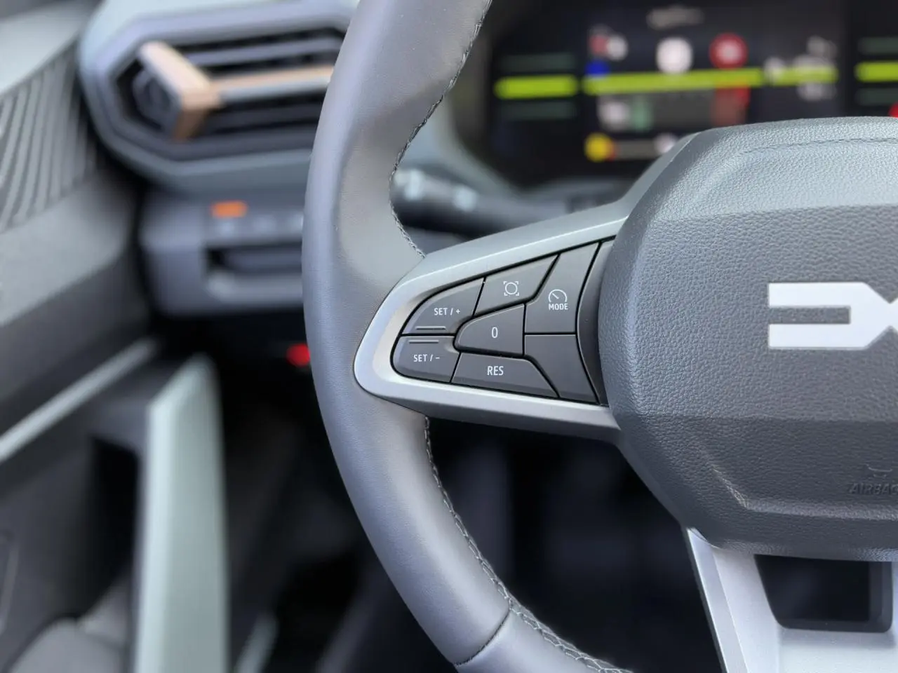 Gros plan sur le volant gris du Dacia Duster 2025 avec commandes intégrées et tableau de bord numérique flou en arrière-plan.