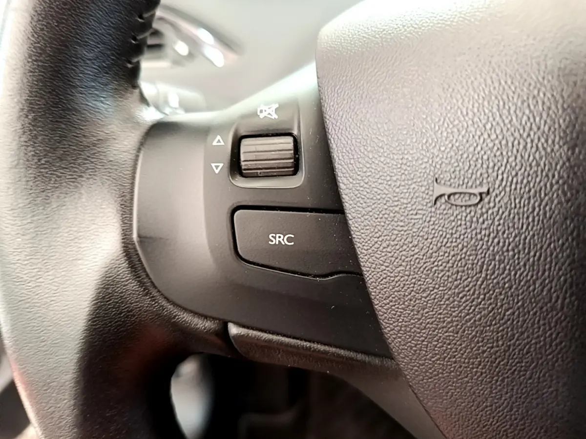 Gros plan sur les commandes gauche du volant cuir de la Peugeot 208 Puretech 82 Signature 2019, avec bouton SRC et molette sonore.