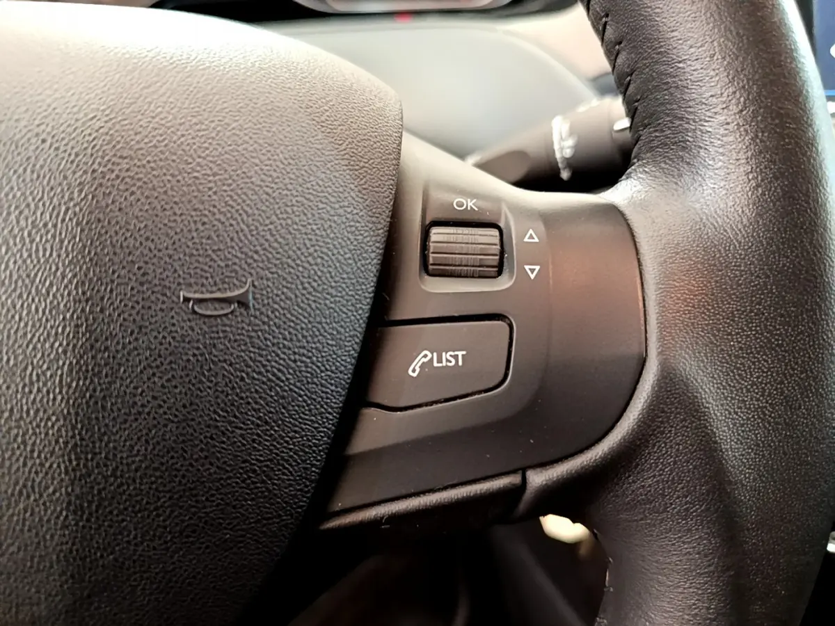 Gros plan sur les commandes du volant cuir de la Peugeot 208 Puretech 82 Signature, version essence blanche de 2019.