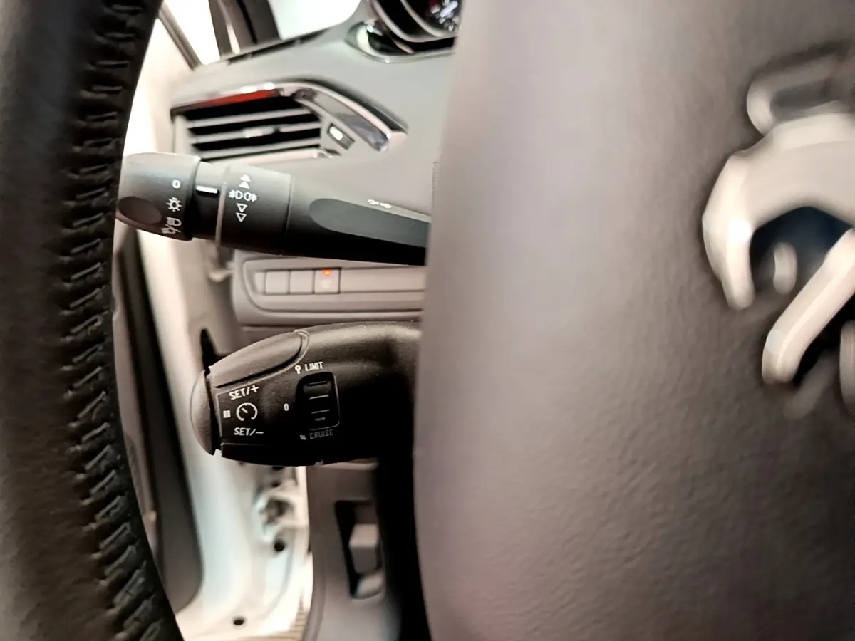 Détail du volant cuir et commandes de régulateur de vitesse sur Peugeot 208 blanc, vue côté gauche intérieur.