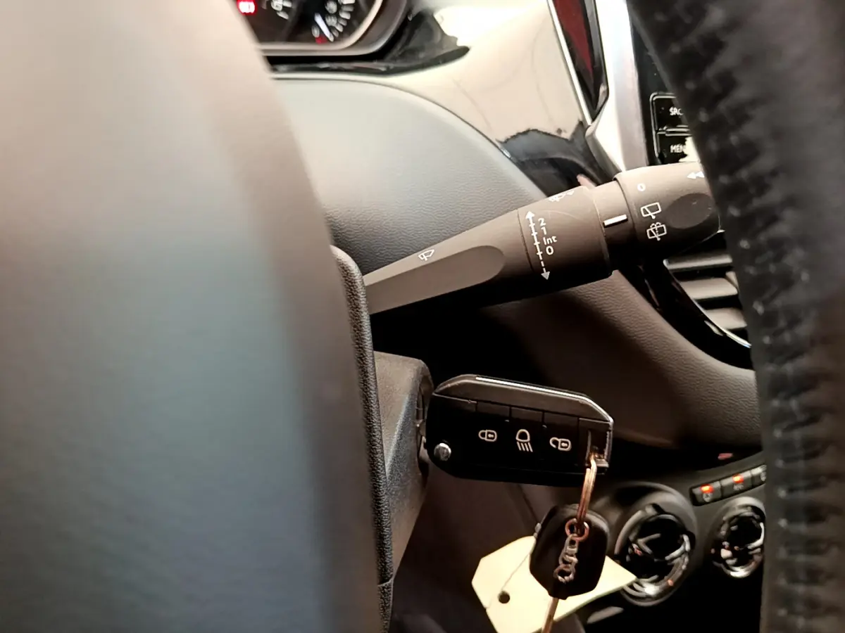 Gros plan sur la clé insérée dans le contacteur et la commande d'essuie-glace du tableau de bord d'une Peugeot 208 blanche.