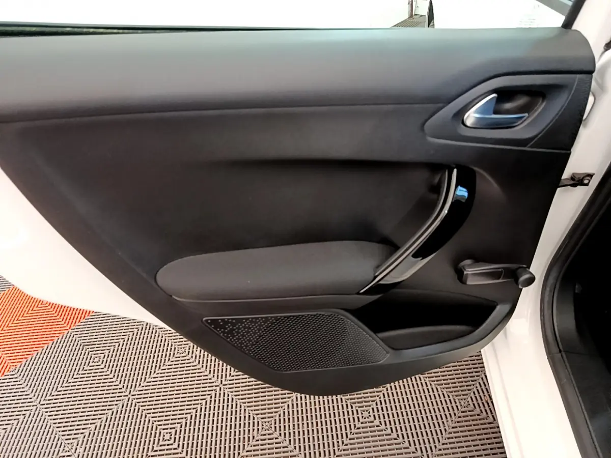 Vue rapprochée de la porte avant gauche noire d’une Peugeot 208 blanche, mettant en valeur la poignée intérieure chromée.