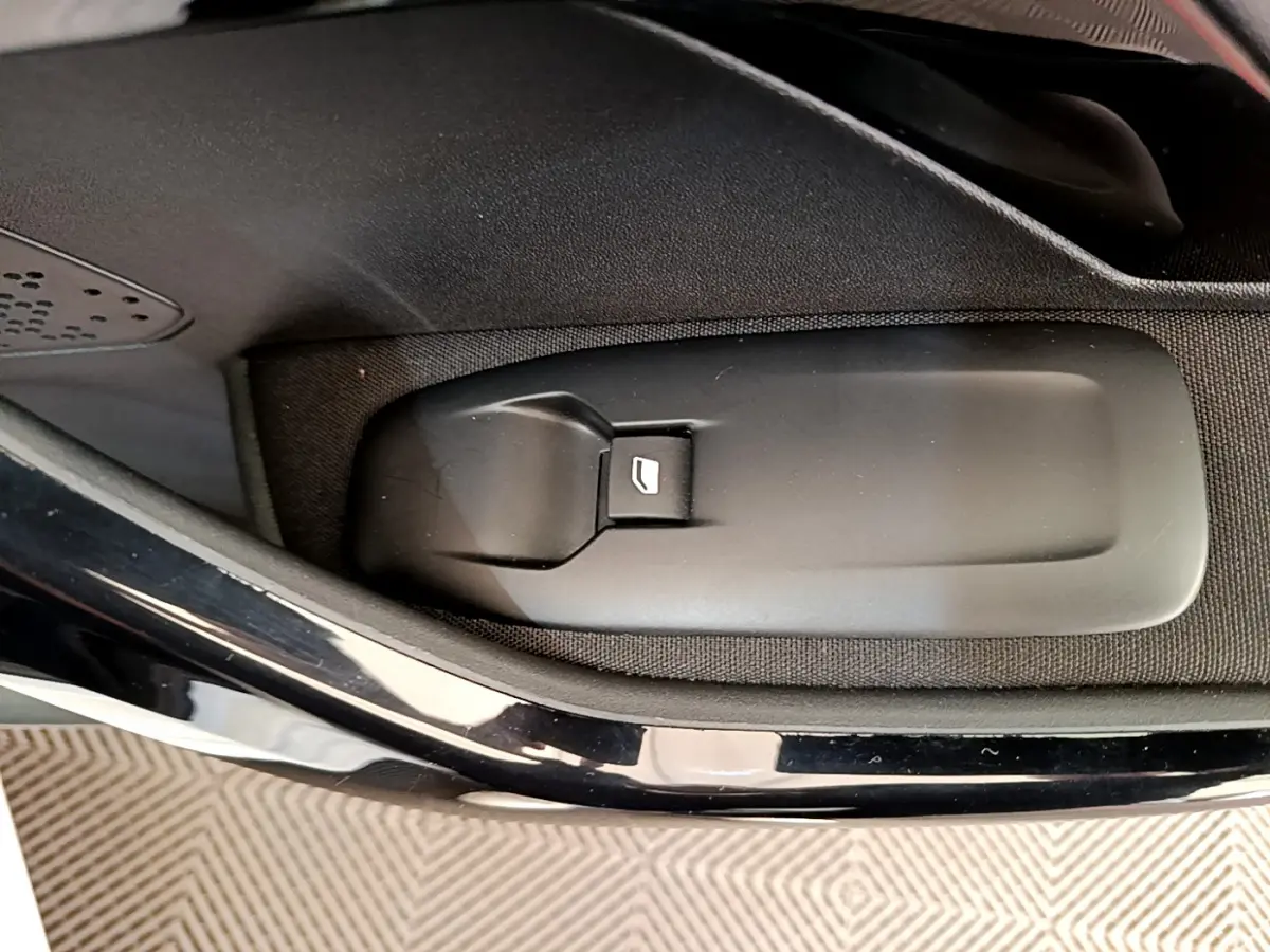 Bouton de commande de lève-vitre électrique sur la porte intérieure d'une Peugeot 208 blanche Puretech 82 Signature.