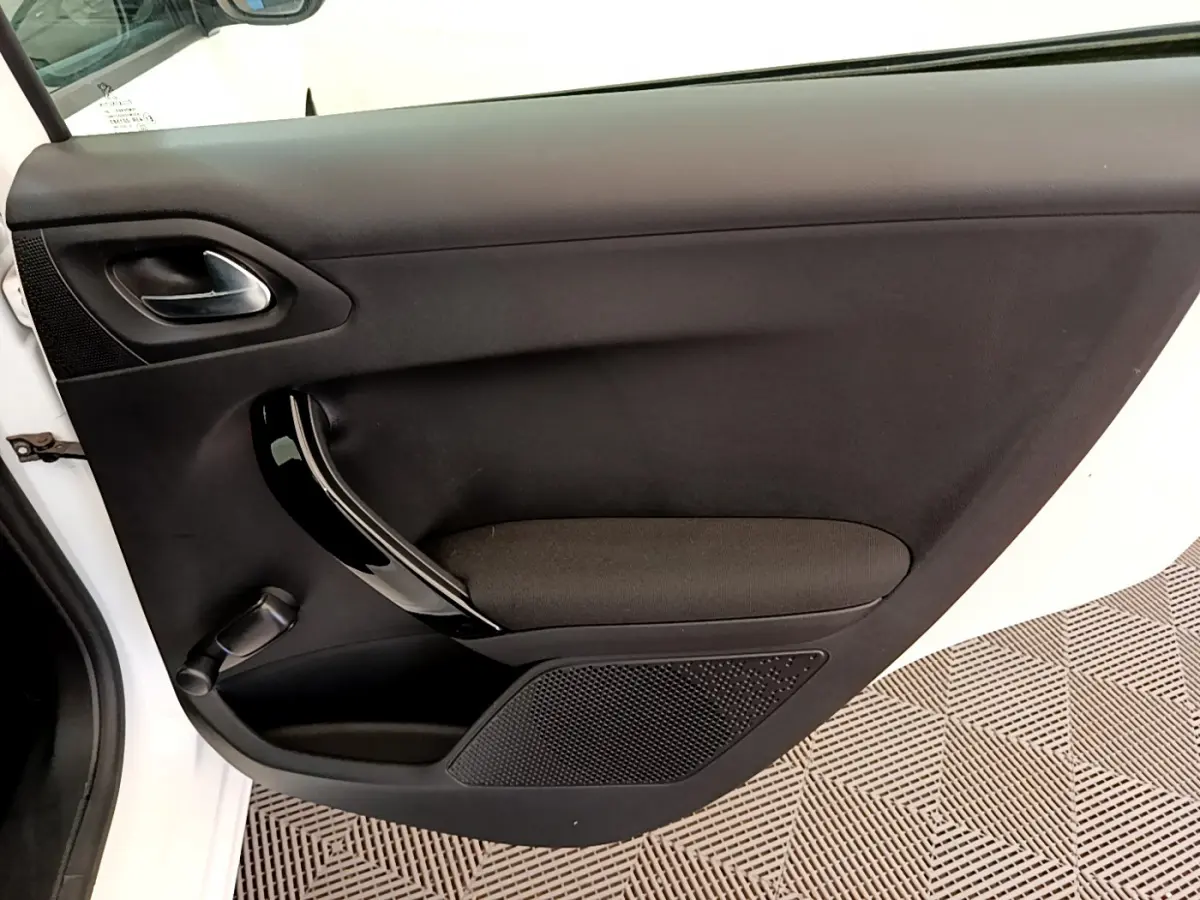 Vue intérieure de la porte côté gauche d'une Peugeot 208 blanche, avec poignée noire brillante et tissu noir.