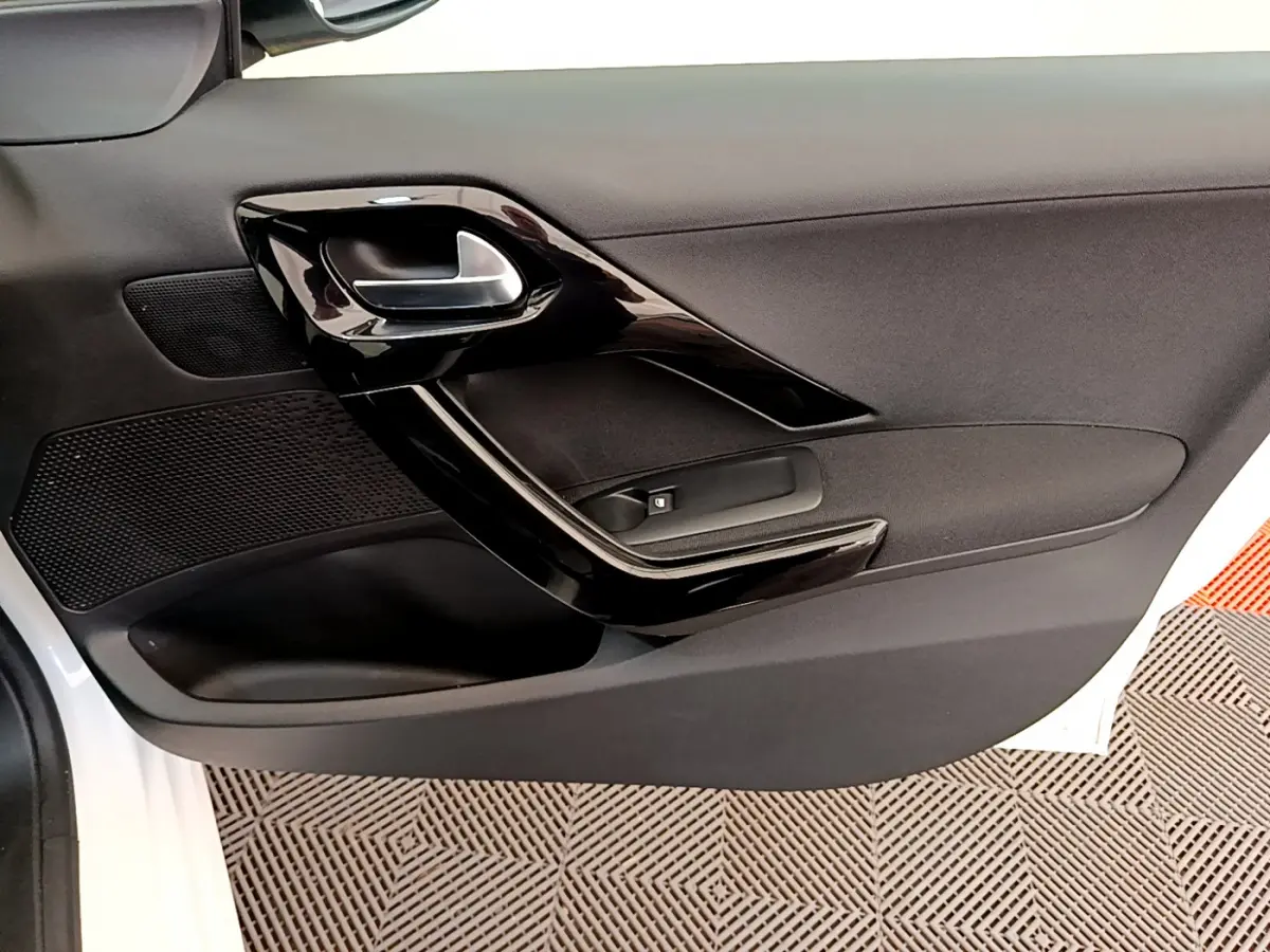Gros plan sur la porte côté gauche blanche d'une Peugeot 208 Puretech 82 Signature avec poignée intérieure noire brillante.