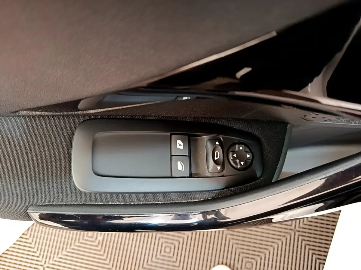 Gros plan sur les commandes électriques des vitres côté conducteur d'une Peugeot 208 blanche, finition Signature.