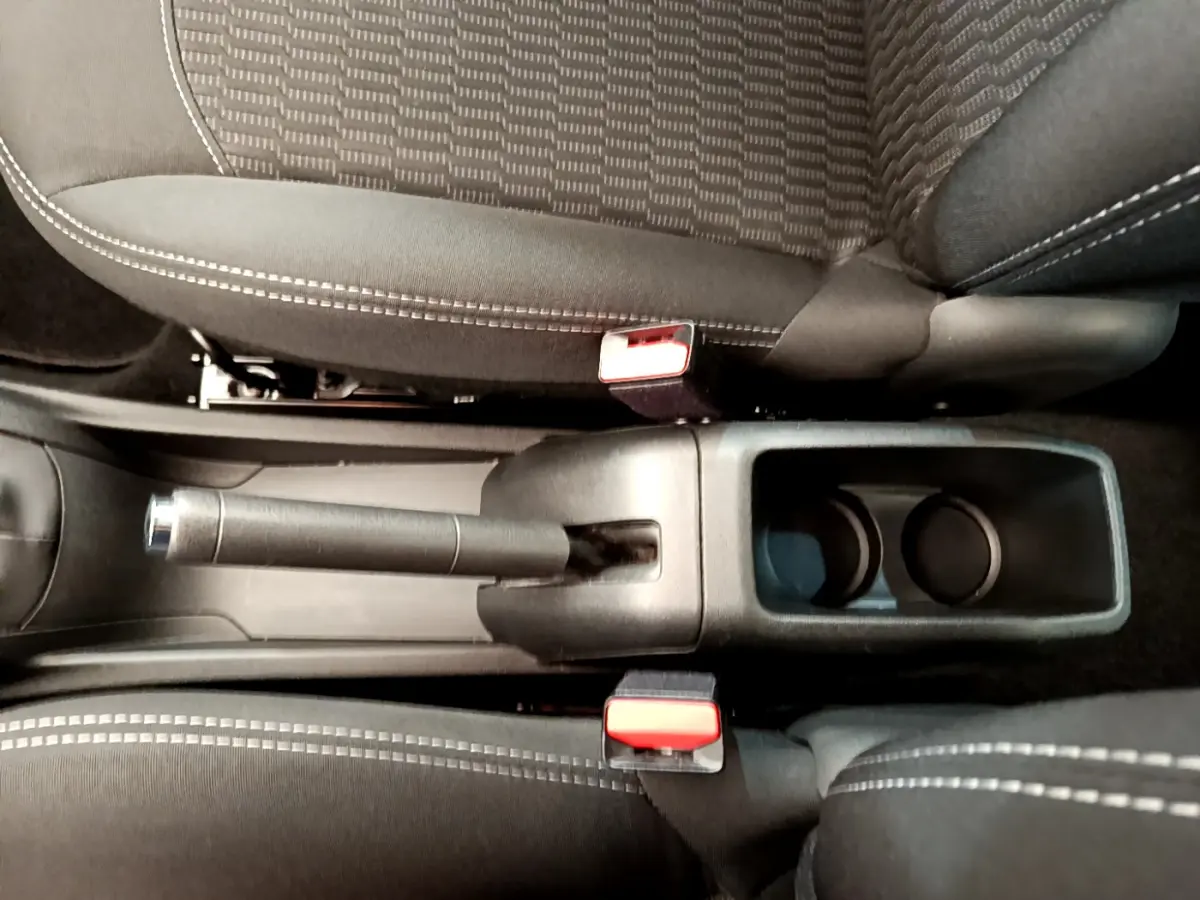 Gros plan sur le frein à main manuel et porte-gobelets entre les sièges noirs à surpiqûres blanches d'une Peugeot 208 blanche.