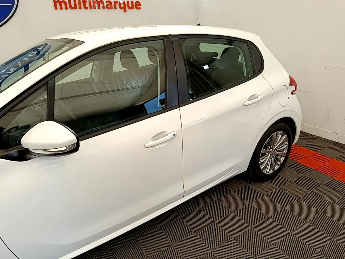 Profil côté droit de la Peugeot 208 Puretech 82 Signature blanche, avec rétroviseurs chromés et jantes alliage visibles.
