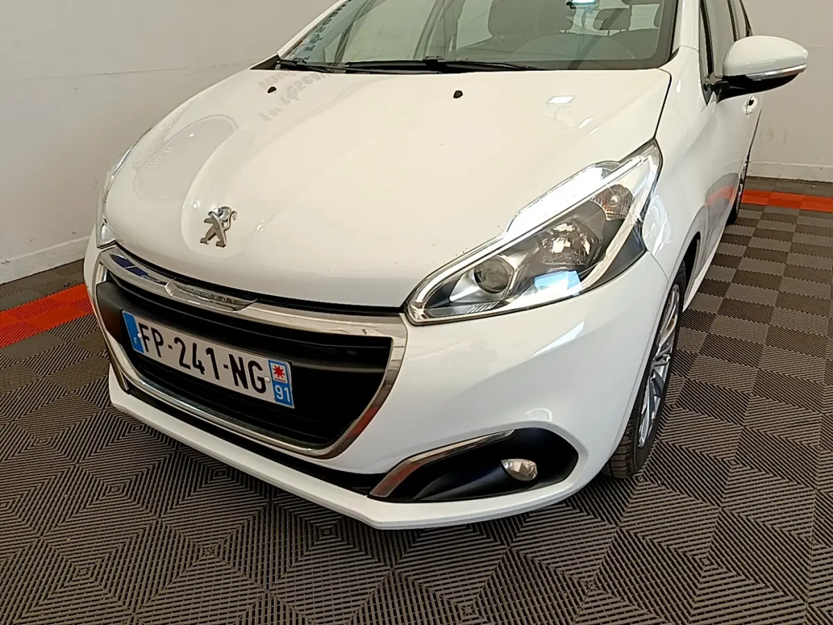 Peugeot 208 Puretech 82 Signature blanc vue 3/4 avant droit, avec phares et antibrouillards visibles.