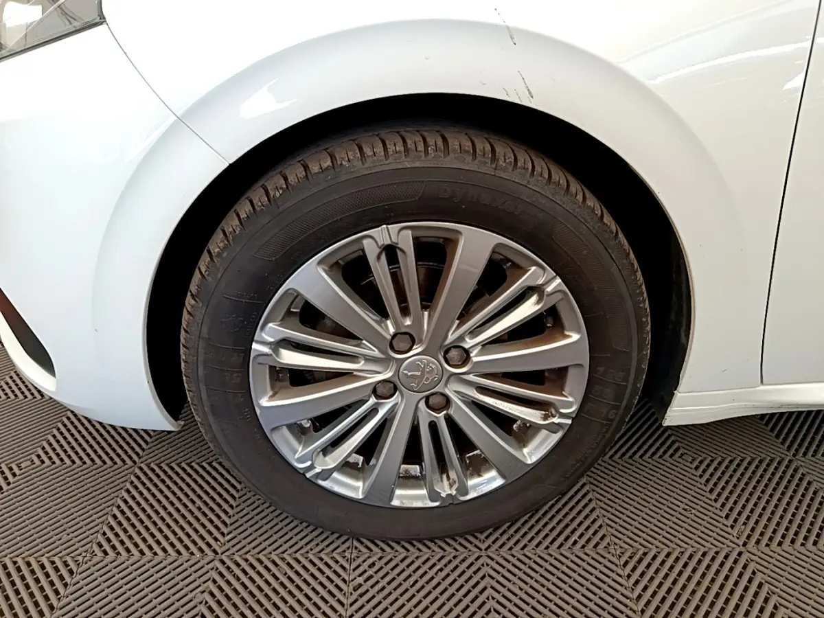 Gros plan sur la roue avant gauche d'une Peugeot 208 blanche, avec jante alliage au design moderne.