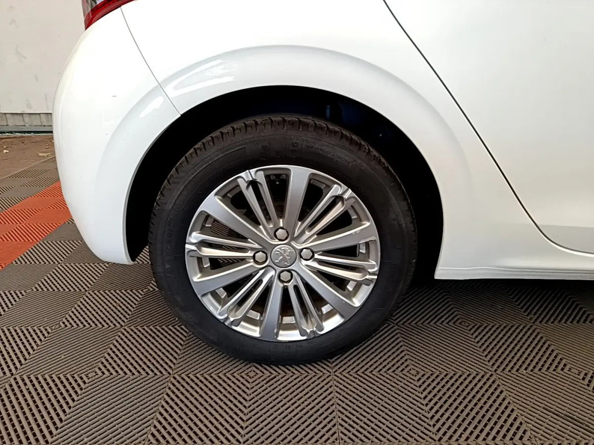 Gros plan sur la roue arrière droite d'une Peugeot 208 blanche, mettant en valeur la jante alliage élégante.