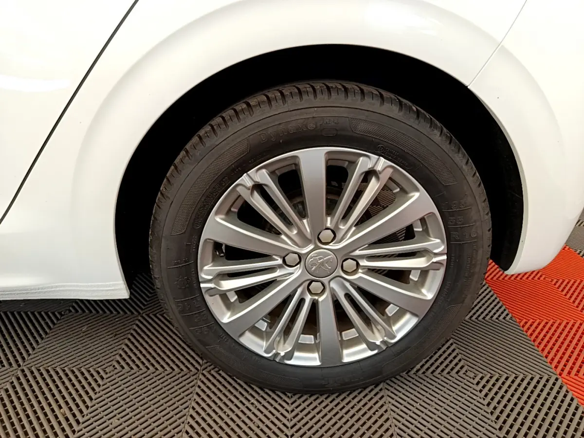 Gros plan sur la roue arrière droite d'une Peugeot 208 blanche avec jante alliage multi-branches.