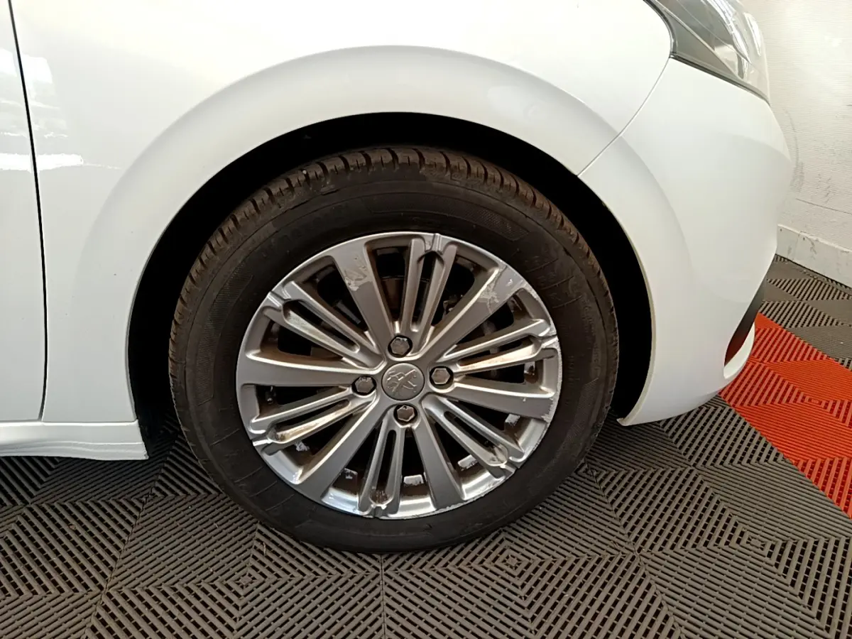 Gros plan sur la roue avant gauche de la Peugeot 208 Puretech 82 Signature blanche de 2019 avec jante alliage.