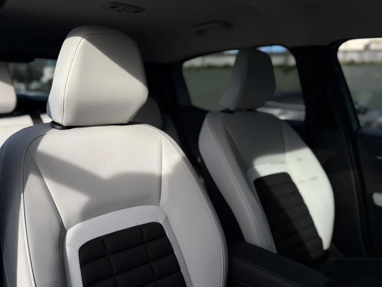 Gros plan sur les sièges avant gris clair et noir de la Citroën C3 Aircross Hybrid 2025, intérieur lumineux.