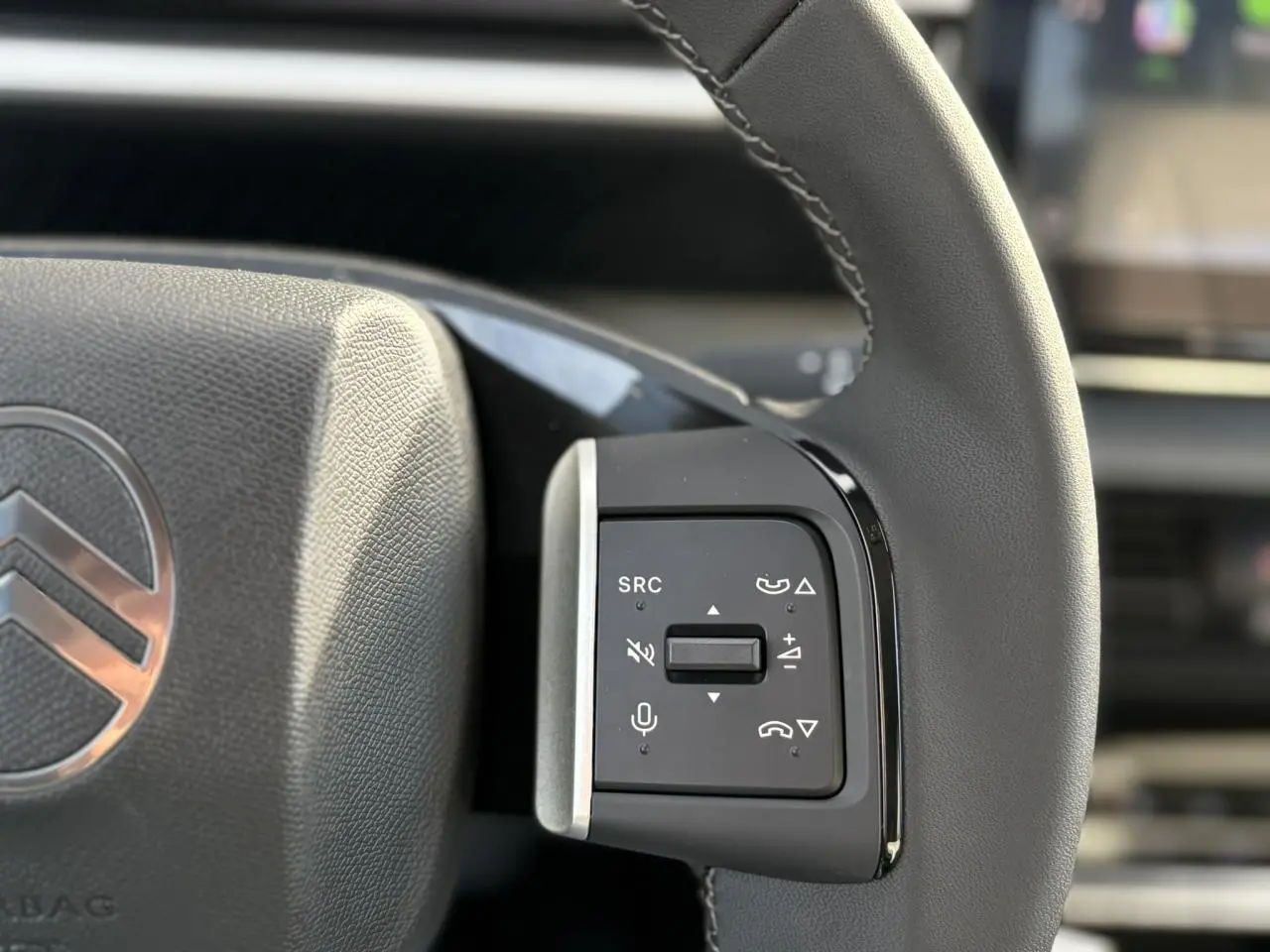 Gros plan sur les commandes multifonctions noires à droite du volant gris du Citroën C3 Aircross Hybrid 2025.