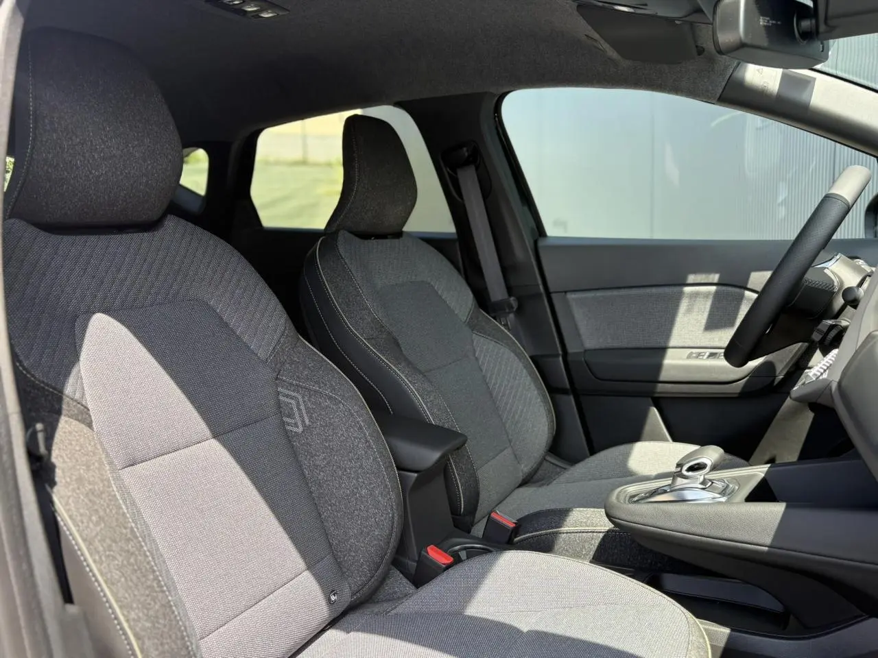 Intérieur du Renault Captur 2025 en vue latérale droite, sièges tissu gris avec console centrale et volant multifonctions.