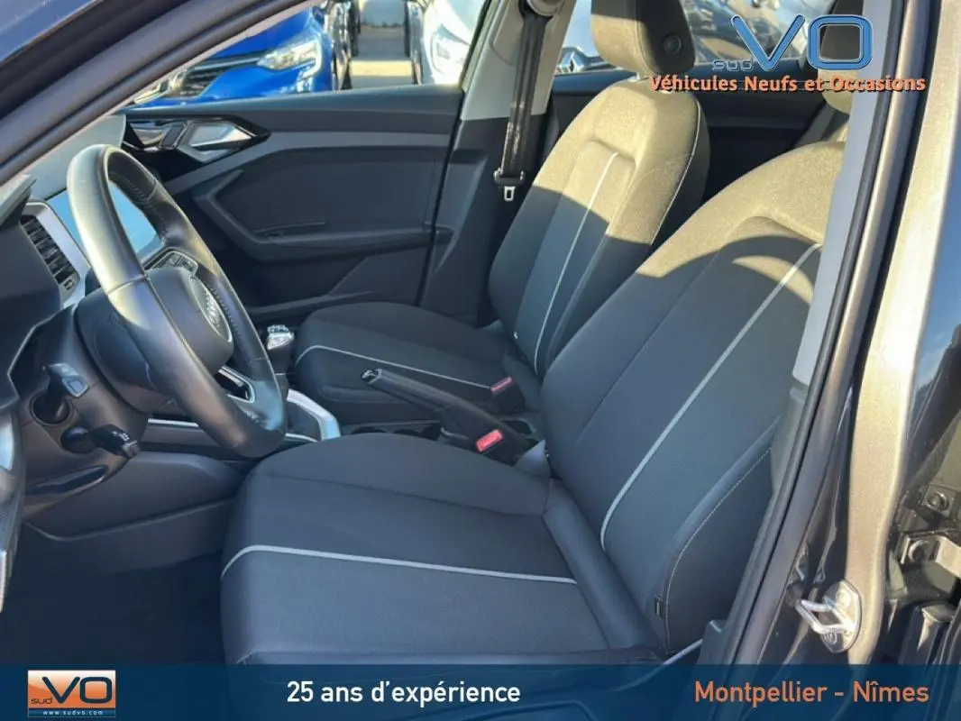 Intérieur avant de l'Audi A1 Sportback gris foncé, sièges sport noirs avec surpiqûres claires et volant cuir visible côté gauche.
