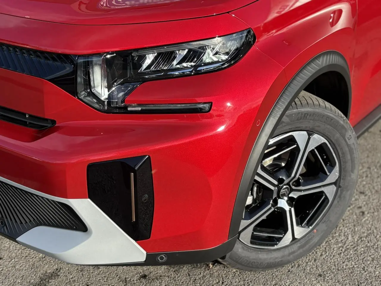 Gros plan sur l'avant droit rouge Elixir du Citroën C3 Aircross 2025, mettant en valeur le phare LED et la jante alliage noire.