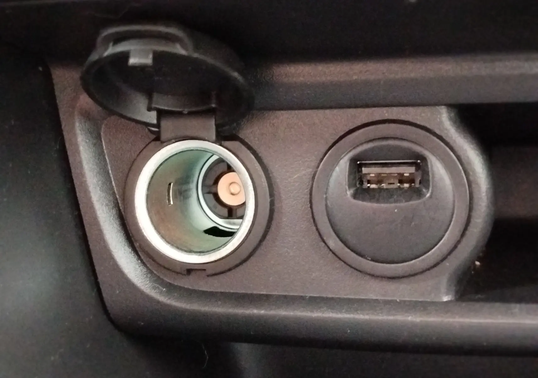 Gros plan intérieur sur la prise allume-cigare ouverte et un port USB à côté dans une Peugeot 208 noire.