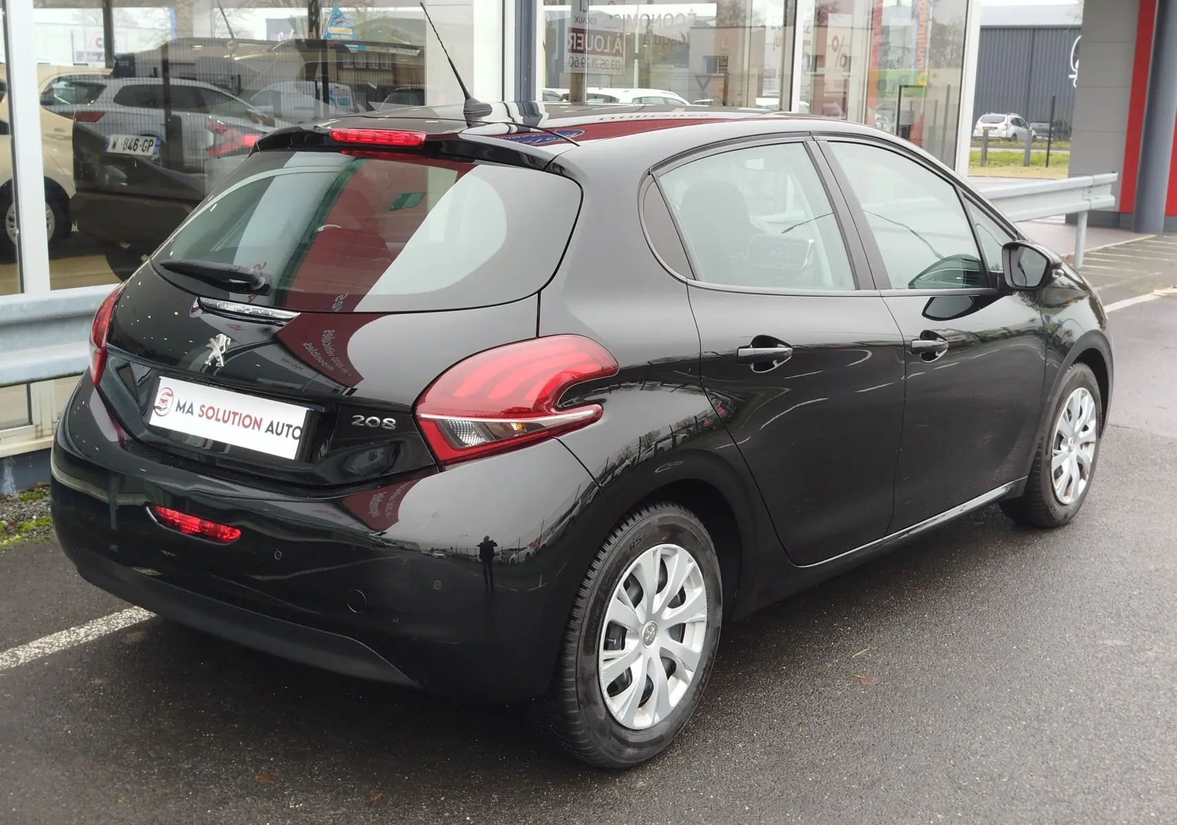 Vue 3/4 arrière droite d'une Peugeot 208 noire Perla Nera de 2019, avec feux arrière distinctifs et jantes argentées.
