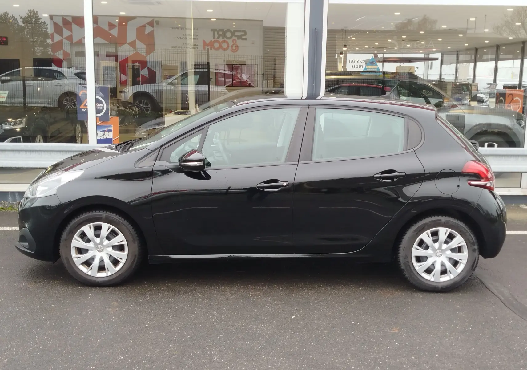Peugeot 208 noir Perla Nera vue de profil côté gauche, stationnée devant une vitrine de concession.