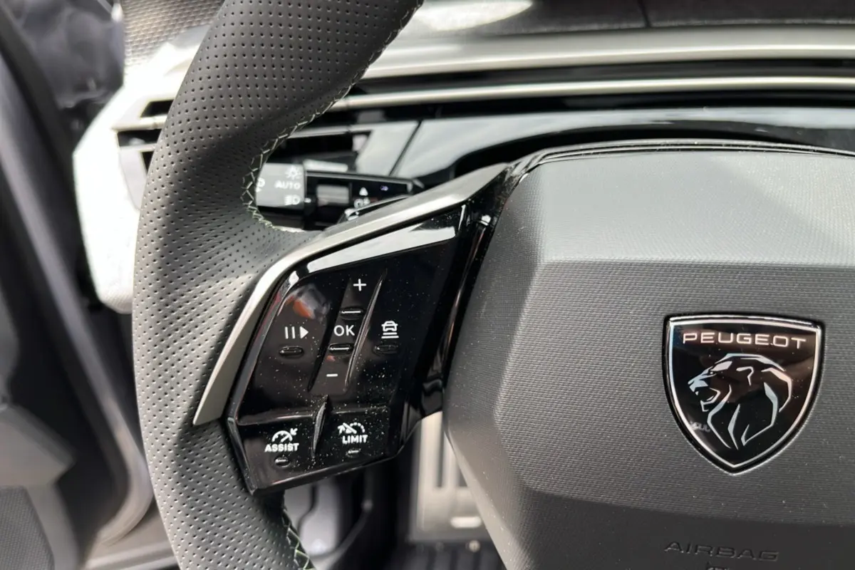 Gros plan sur le volant cuir perforé du Peugeot 5008 Hybrid 145 GT, avec commandes multifonctions et logo lion noir.