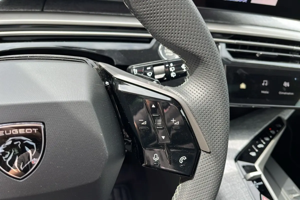 Gros plan sur le volant cuir perforé du Peugeot 5008 Hybrid 145 GT avec commandes multifonctions et logo lion.
