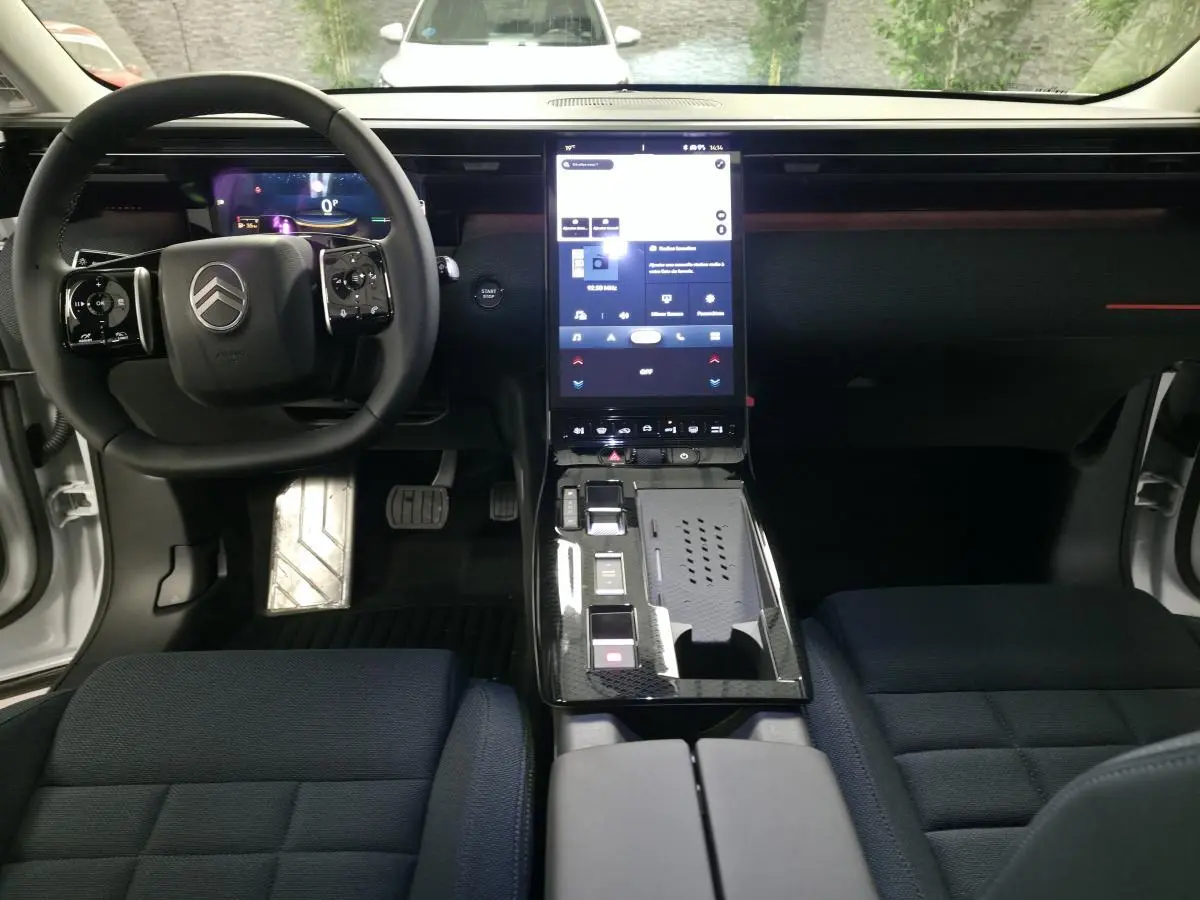 Vue intérieure avant du Citroën C5 Aircross blanc, tableau de bord noir avec écran tactile vertical et sièges tissu bleu.