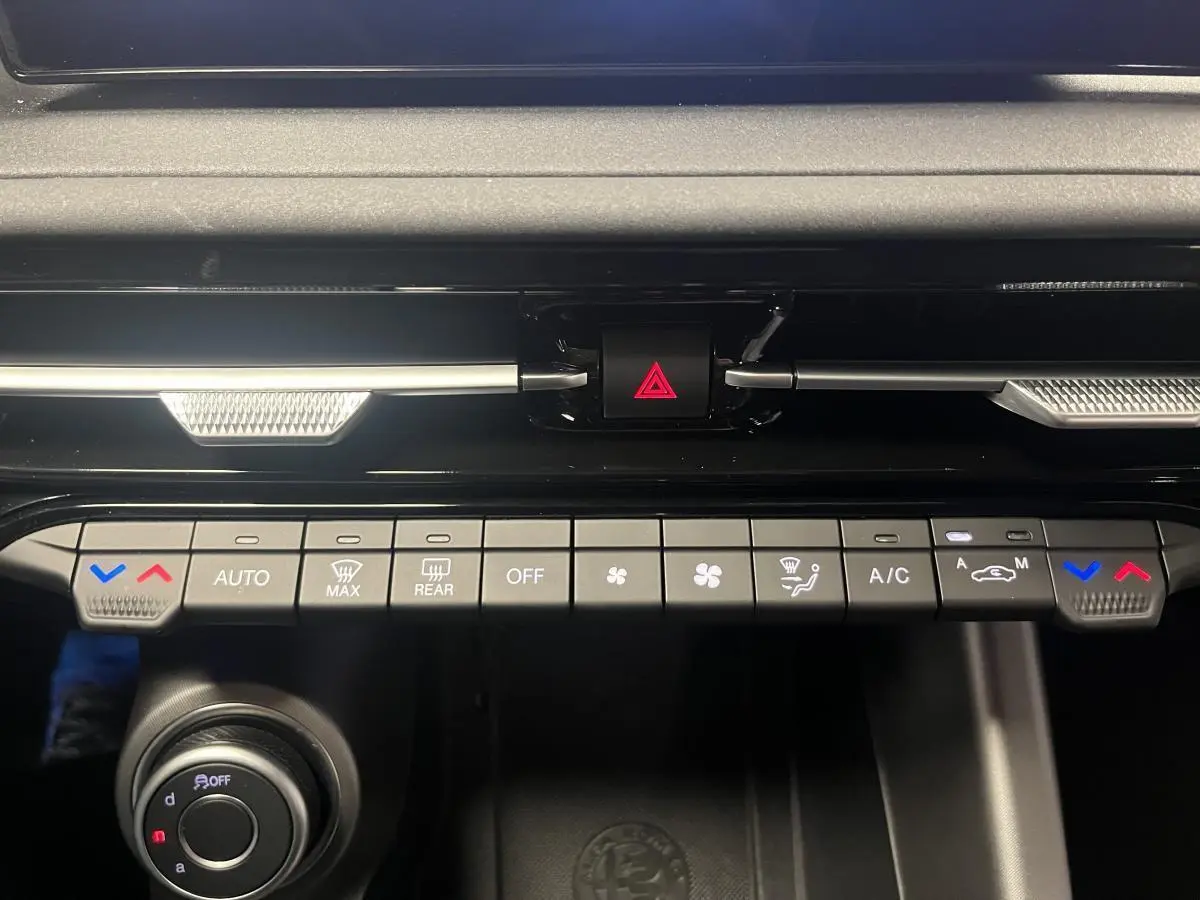 Gros plan sur la console centrale de l'Alfa Romeo Tonale gris foncé, montrant les commandes de climatisation et le bouton de warning.