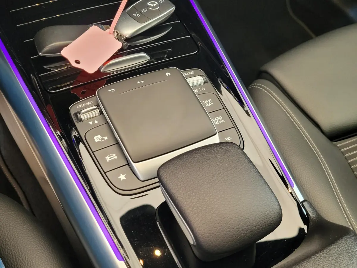 Gros plan sur la console centrale noire brillante du Mercedes GLA 200 D bleu, avec touches de commande et éclairage violet.