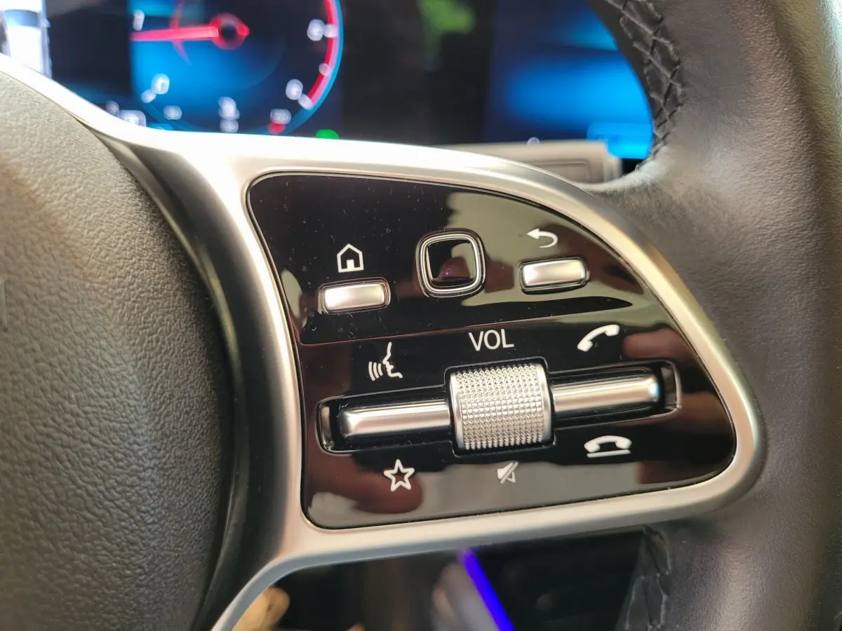 Gros plan sur les commandes de volume et fonctions vocales au volant cuir d'une Mercedes GLA 200 D bleu 2022.