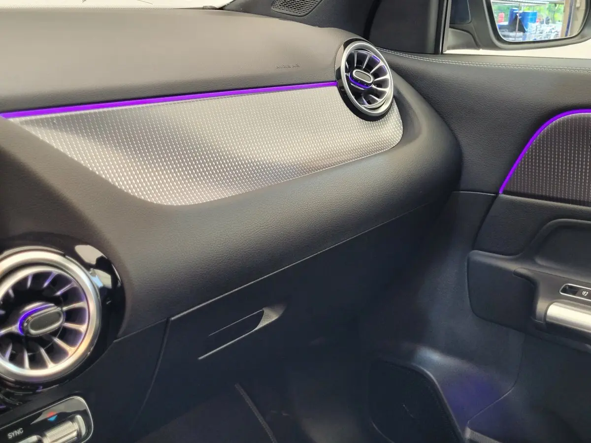 Détail intérieur côté passager du tableau de bord noir et gris avec éclairage d’ambiance violet d’une Mercedes GLA 200 D 2022.