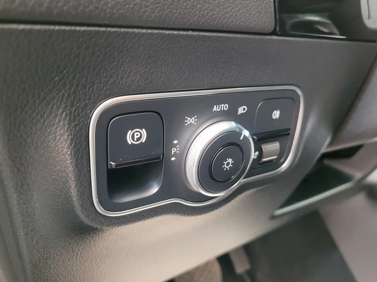 Gros plan sur le panneau de commande des phares et frein à main électrique dans une Mercedes GLA 200 D Business Line bleu 2022.