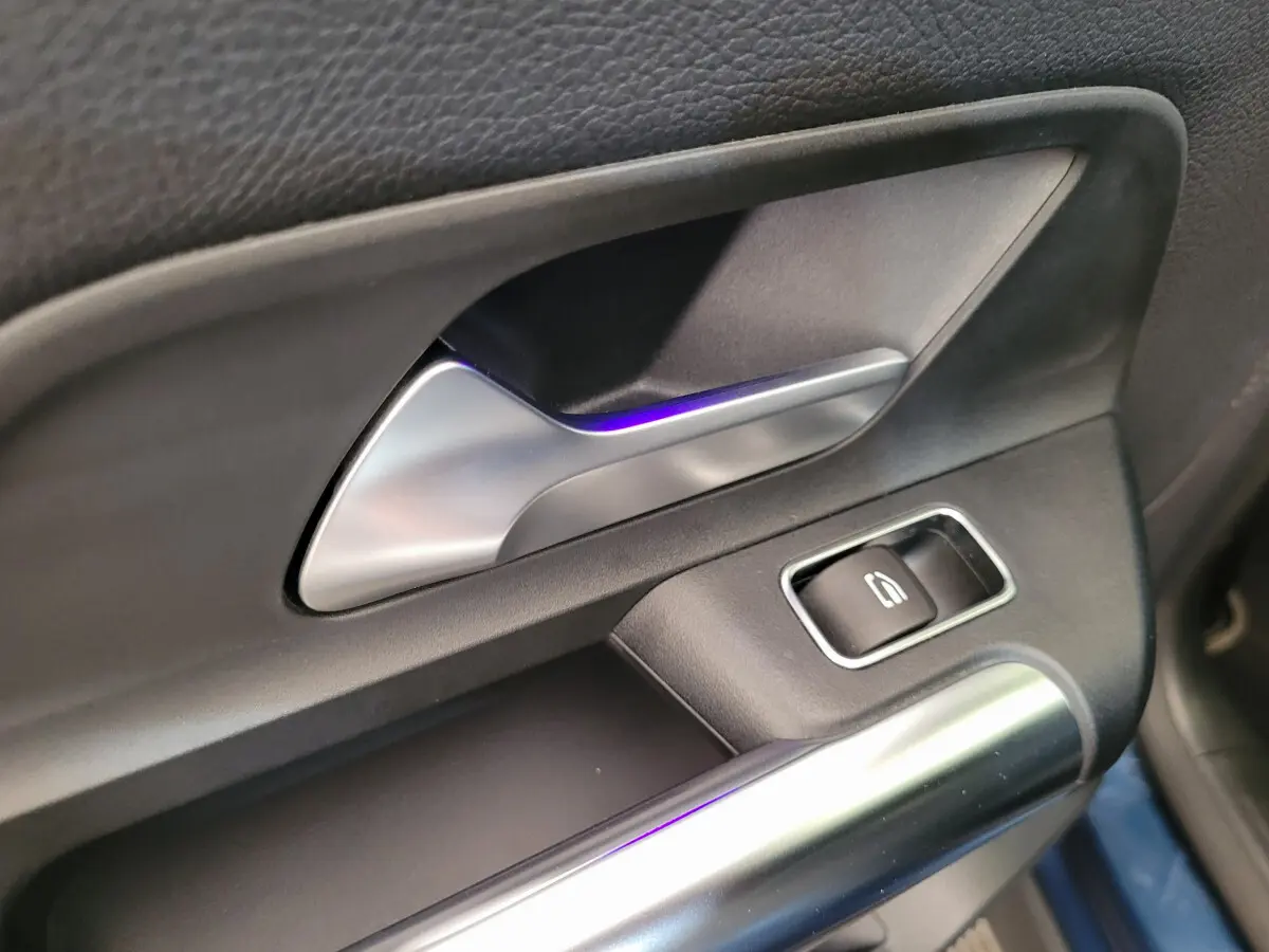 Poignée intérieure côté gauche en métal brossé avec bouton de lève-vitre sur porte d’un Mercedes GLA 200 D bleu 2022.