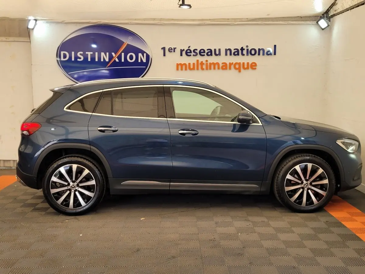 Profil latéral droit d'un Mercedes GLA 200 D Business Line bleu avec jantes alliage et toit chromé en showroom.