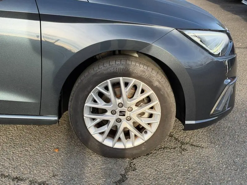 Gros plan sur la roue avant gauche d'une SEAT Ibiza 2025 gris magnétique métallisé avec jante alliage et partie du phare avant visible.