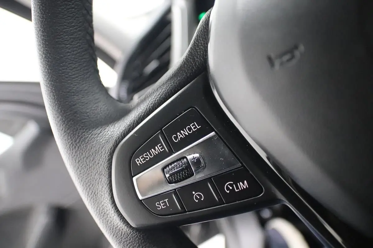 Gros plan sur les commandes du régulateur de vitesse au volant noir d'une BMW Série 1 116d 2023.