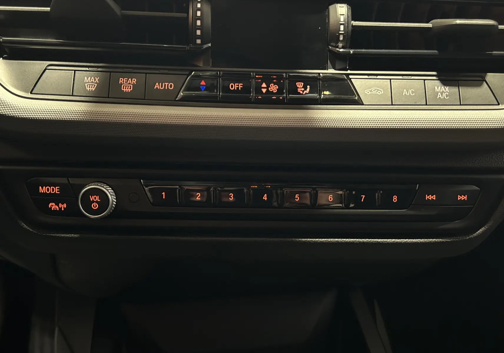 Vue rapprochée du tableau de bord noir de la BMW Série 1 116d 2023, montrant les commandes climatisation et audio rétroéclairées.