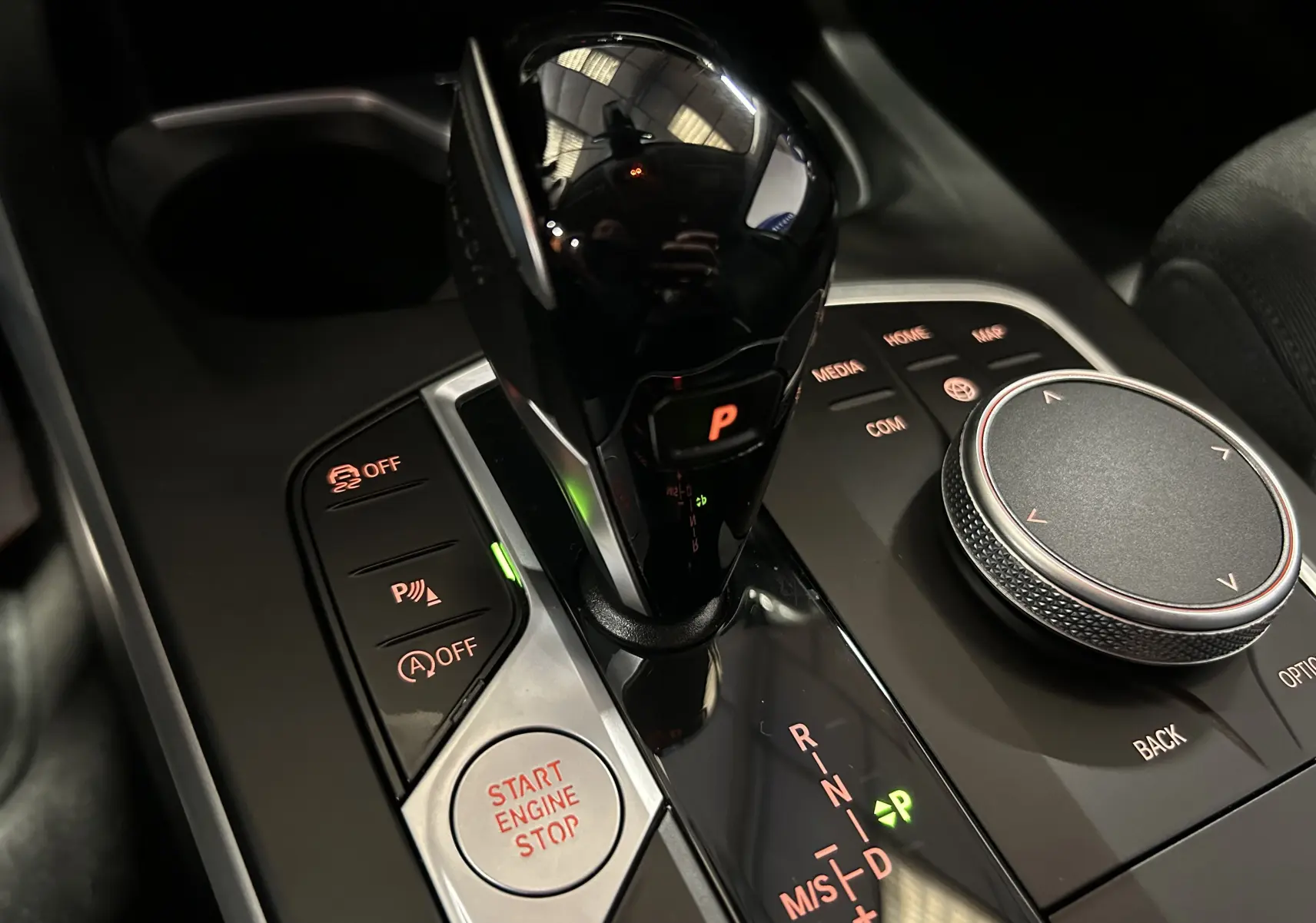 Gros plan sur la console centrale noire de la BMW Série 1 116d 2023, avec levier de vitesse automatique et bouton start/stop éclairés.