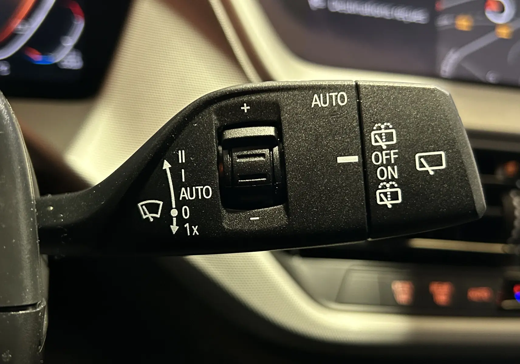 Gros plan sur la commande de l’essuie-glace à gauche du volant dans l’habitacle noir de la BMW Série 1 116d 2023.