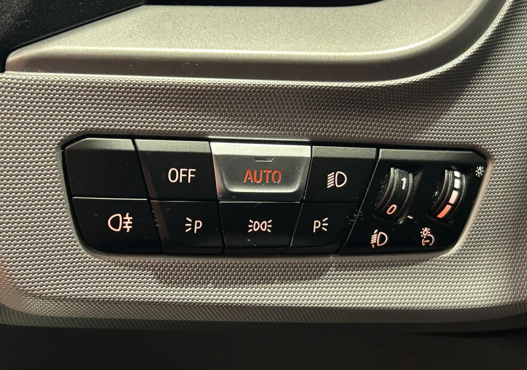 Gros plan sur les commandes d’éclairage intérieures de la BMW Série 1 noire, avec bouton AUTO en surbrillance rouge.