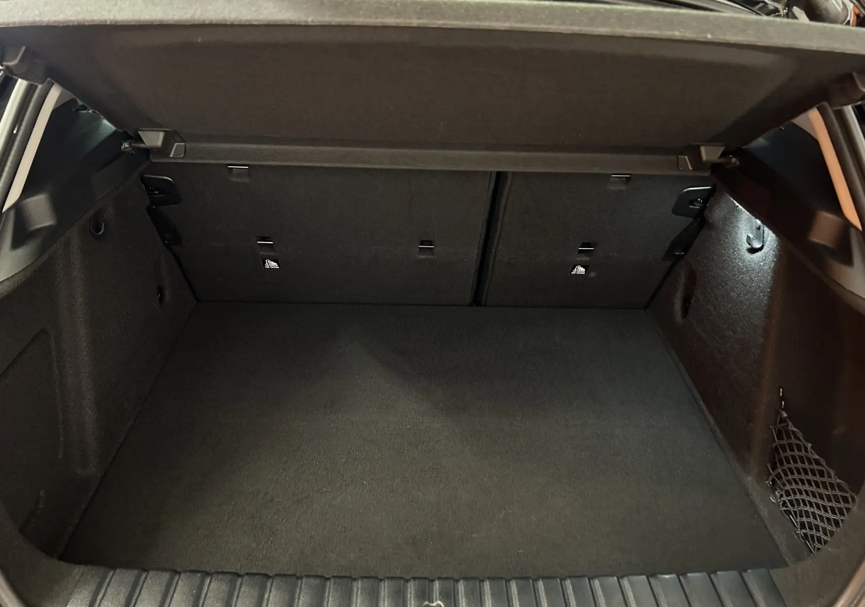 Coffre ouvert en vue plongeante d'une BMW Série 1 116d noire, montrant un espace de chargement propre et bien éclairé.