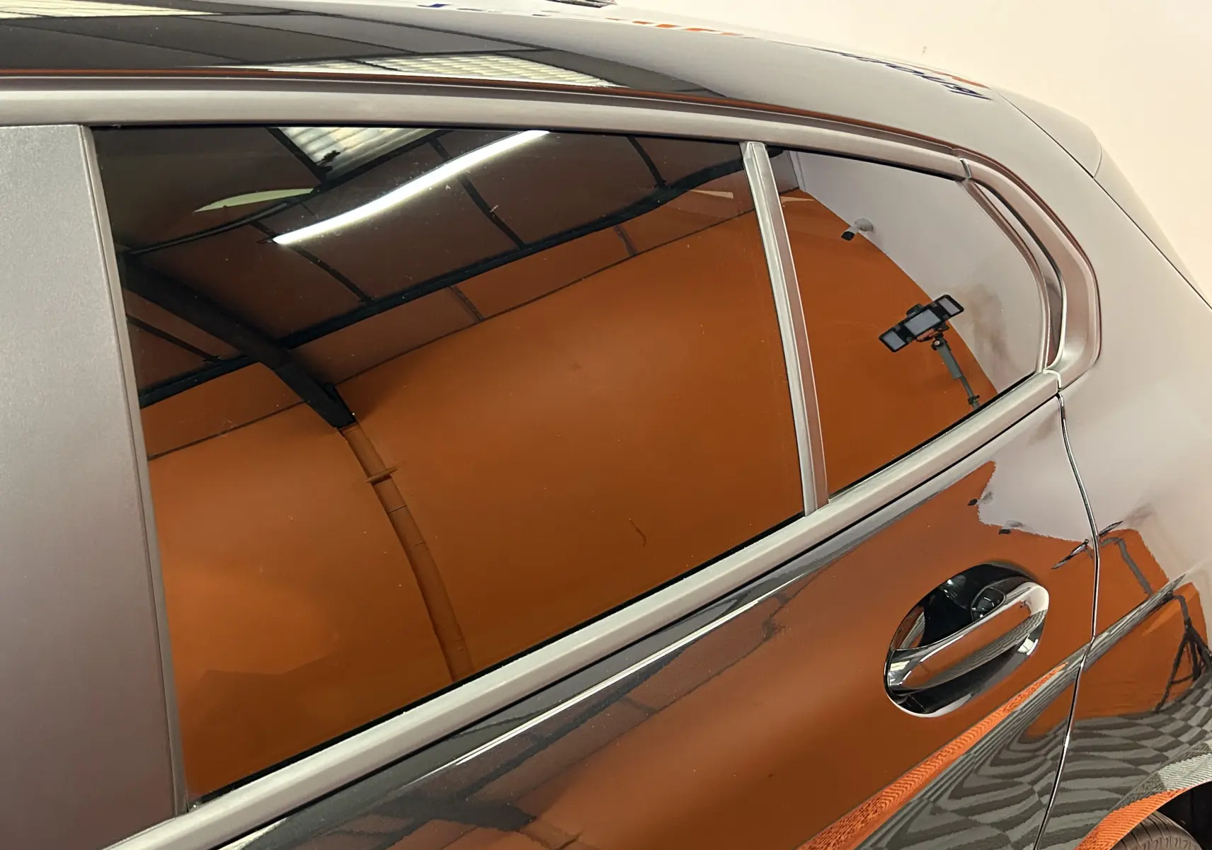 Gros plan sur la porte arrière droite noire brillante d'une BMW Série 1 116d 2023 avec reflet d'éclairage intérieur.