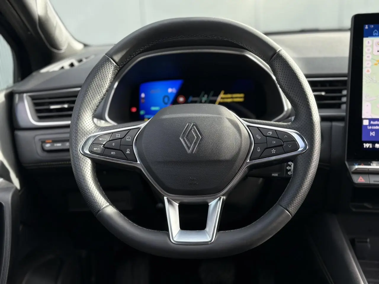 Volant en cuir noir perforé de la Renault SYMBIOZ 2025, avec commandes intégrées et tableau de bord numérique en arrière-plan.