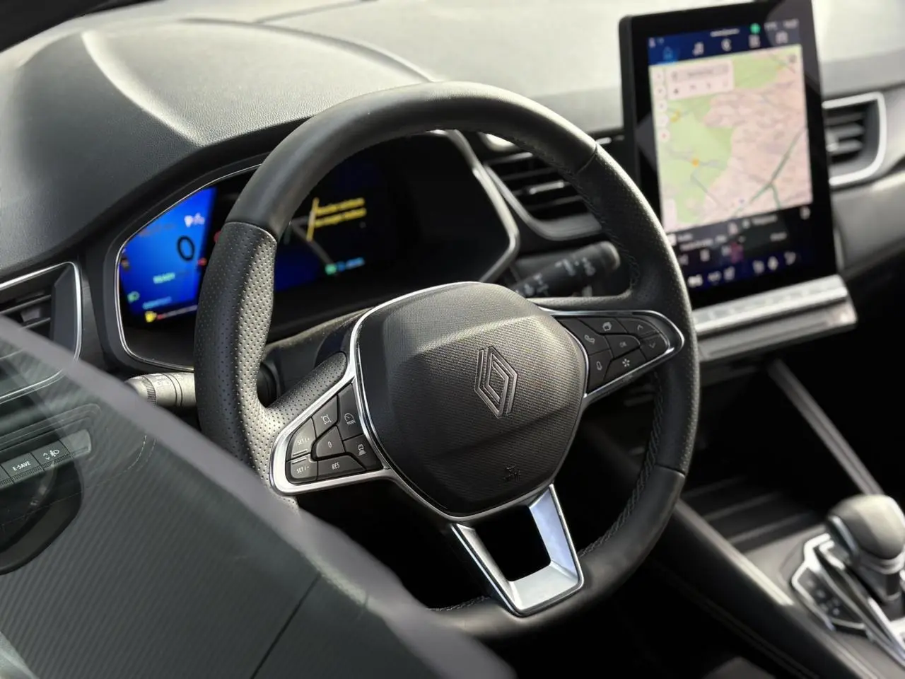 Vue intérieure centrée sur le volant noir perforé de la Renault SYMBIOZ 2025 avec écran tactile de navigation en arrière-plan.